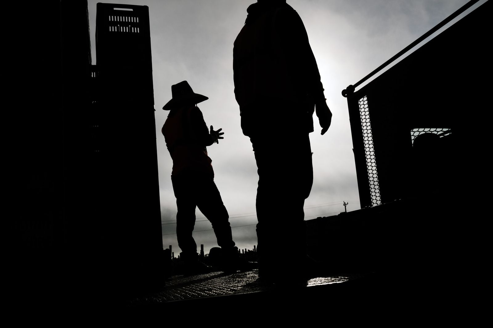 Silhouettes of two men standing in wide-brimmed hats next to a tower of food crates.