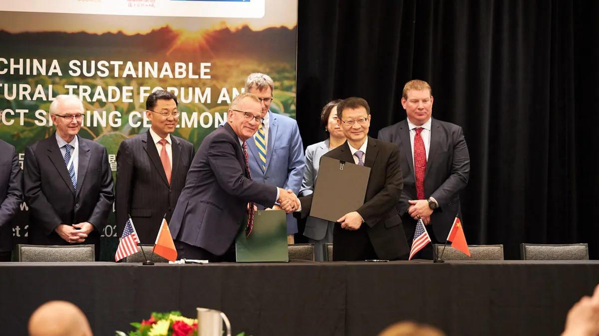 Two men shake hands in front of a panel of people who are clapping