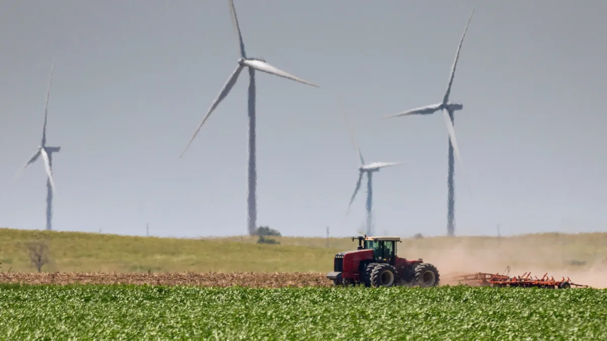 Farmer discing his field as giant wind turbines overlook.