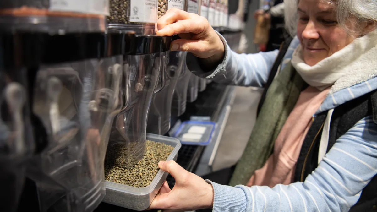 A woman fills a plastic container with lentils from a dispenser