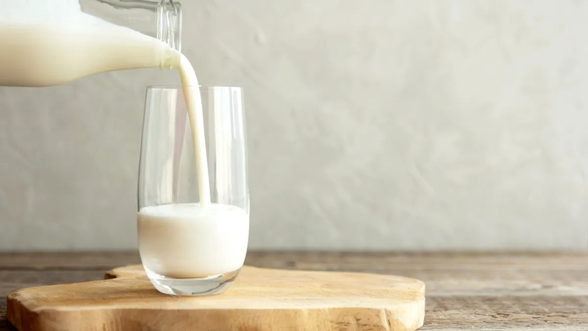 Milk is poured into a clear glass cup.