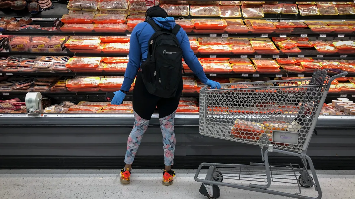 The back of a woman is seen as she looks at the meat section at a grocery store