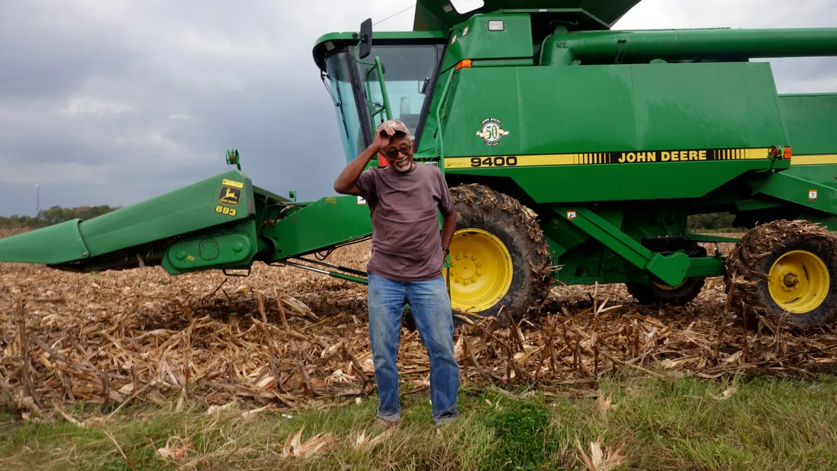 A man adjusts his hat in front of a John Deere tractor