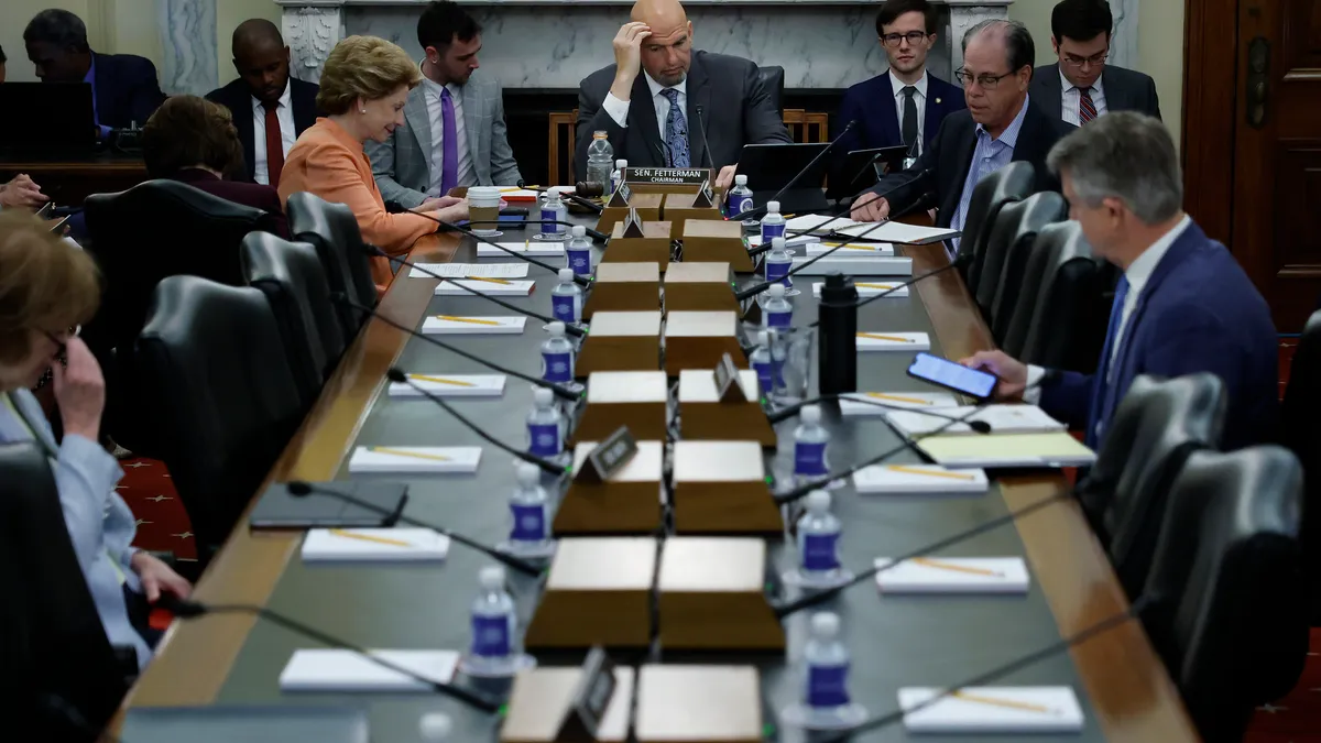 A table of politicians. Sen. John Fetterman sits at the head of the table with a hand on his forehead.