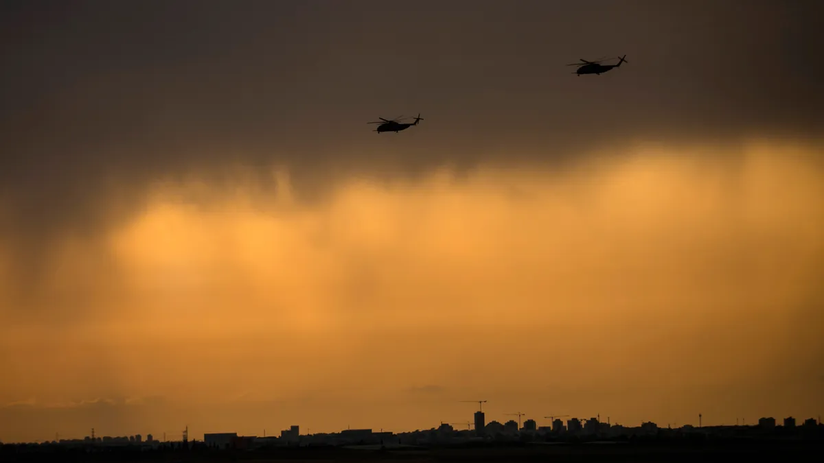 Helicopters fly through smoke-tinged air above a city.