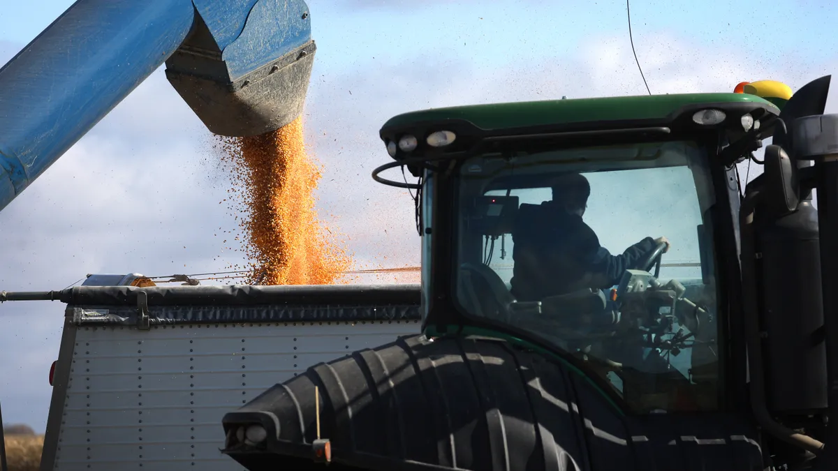 A man in a tractor looks at a grain bin being filled with corn