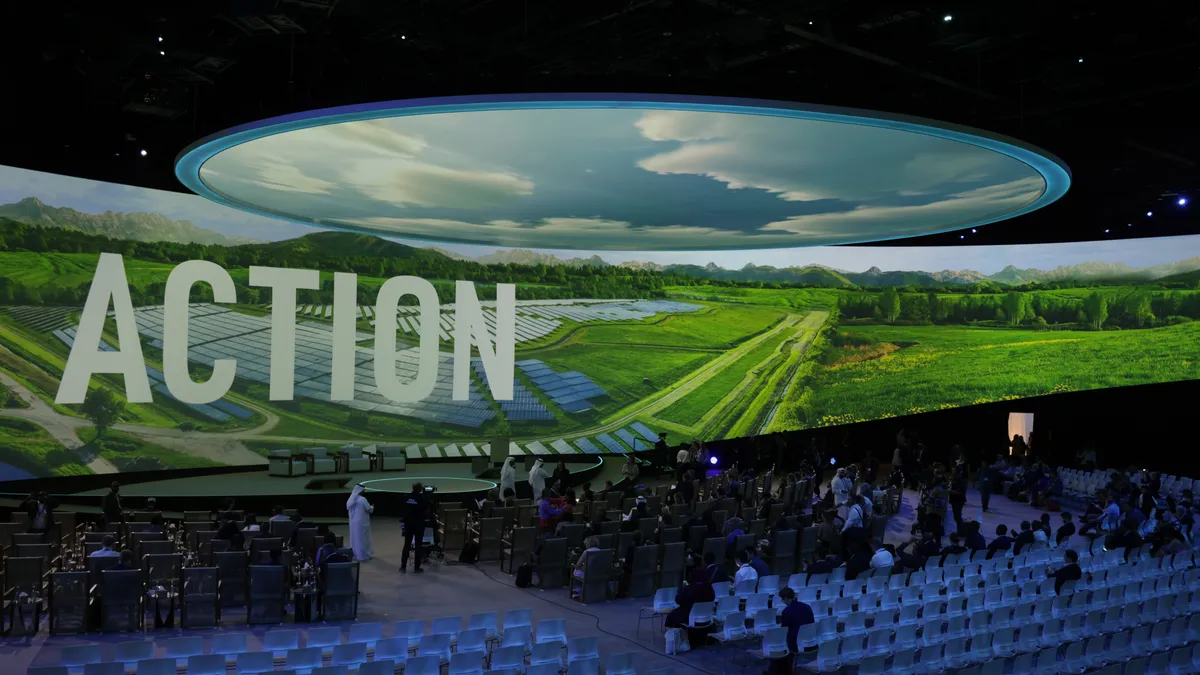 People arrive at a theater where a picture of farmland is projected on a screen with the word "Action."