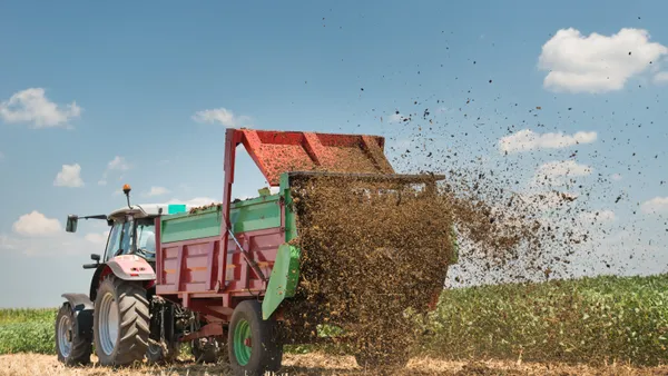 A tractor is seen spreading manure-based fertilizer on a field.